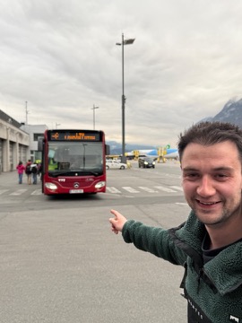 Jordan pointing at a red city bus on the apron at Innsbruck airport, its destination board showing the flight it meets.